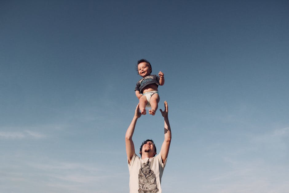 Photo of Man in Raising Baby Under Blue Sky