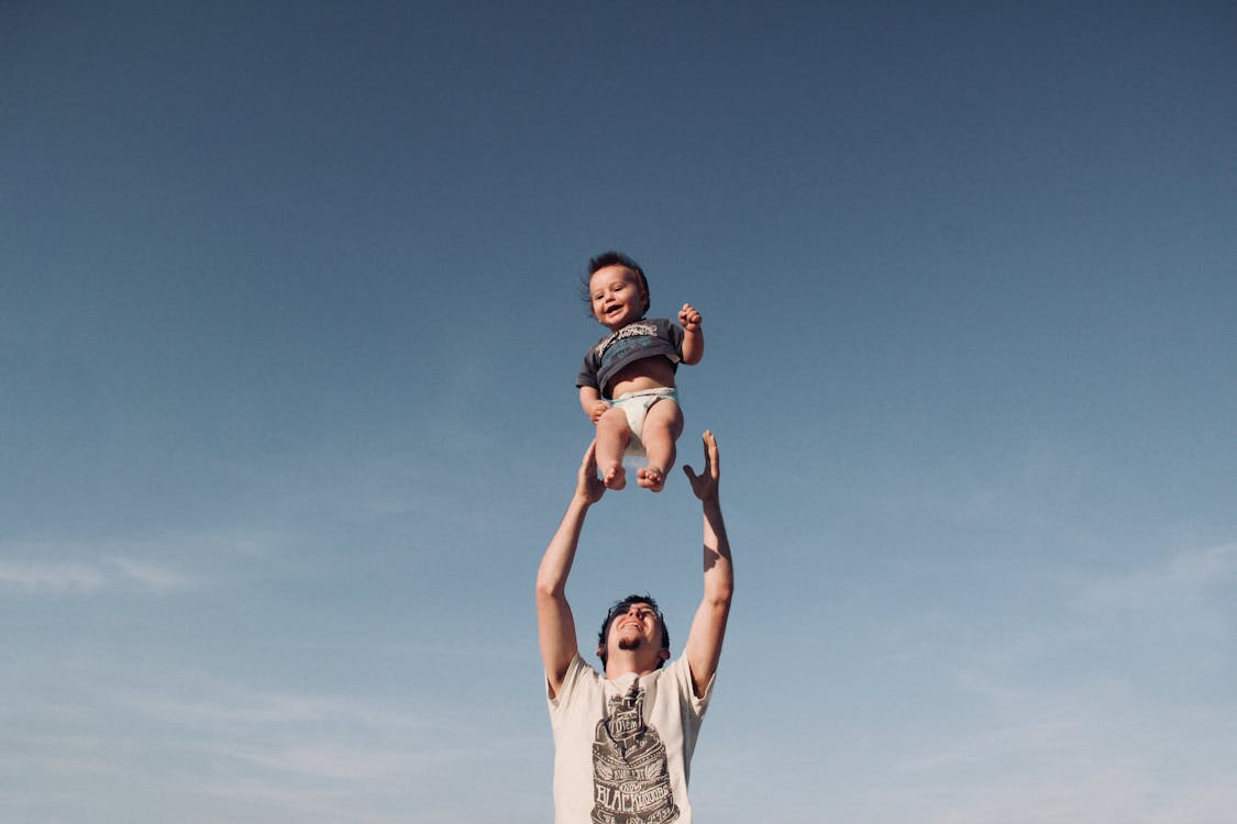 Photo of Man in Raising Baby Under Blue Sky