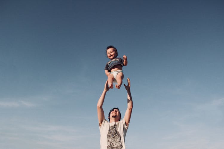 Photo Of Man In Raising Baby Under Blue Sky