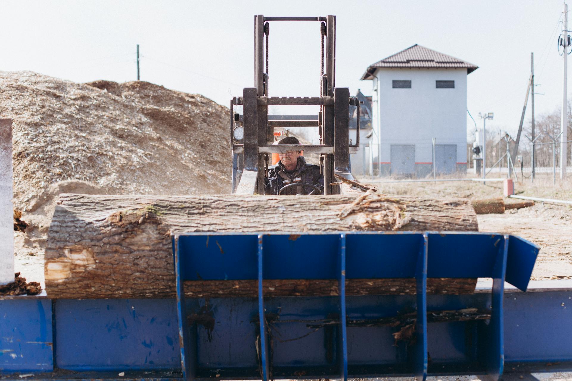 A Man Driving a Tractor Carrying a Tree Trunk