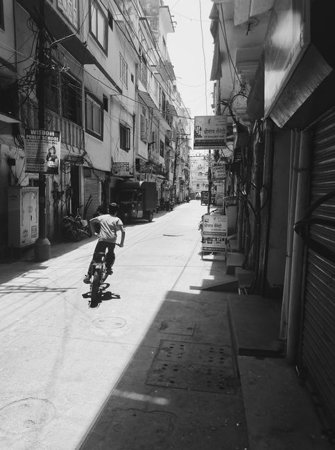 A child rides a bicycle down a narrow urban alley in black and white, showcasing city life.
