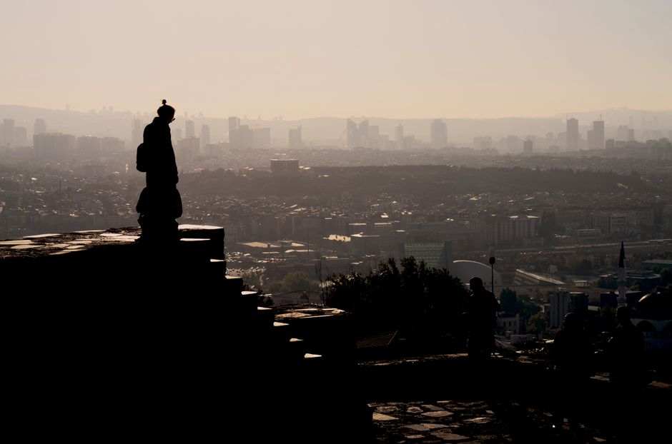 Silhouette of a person overlooking the Ankara skyline with a warm, moody sunset.