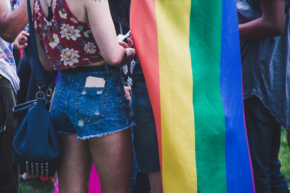 Group of people celebrating at an LGBTQ pride parade with a rainbow flag.