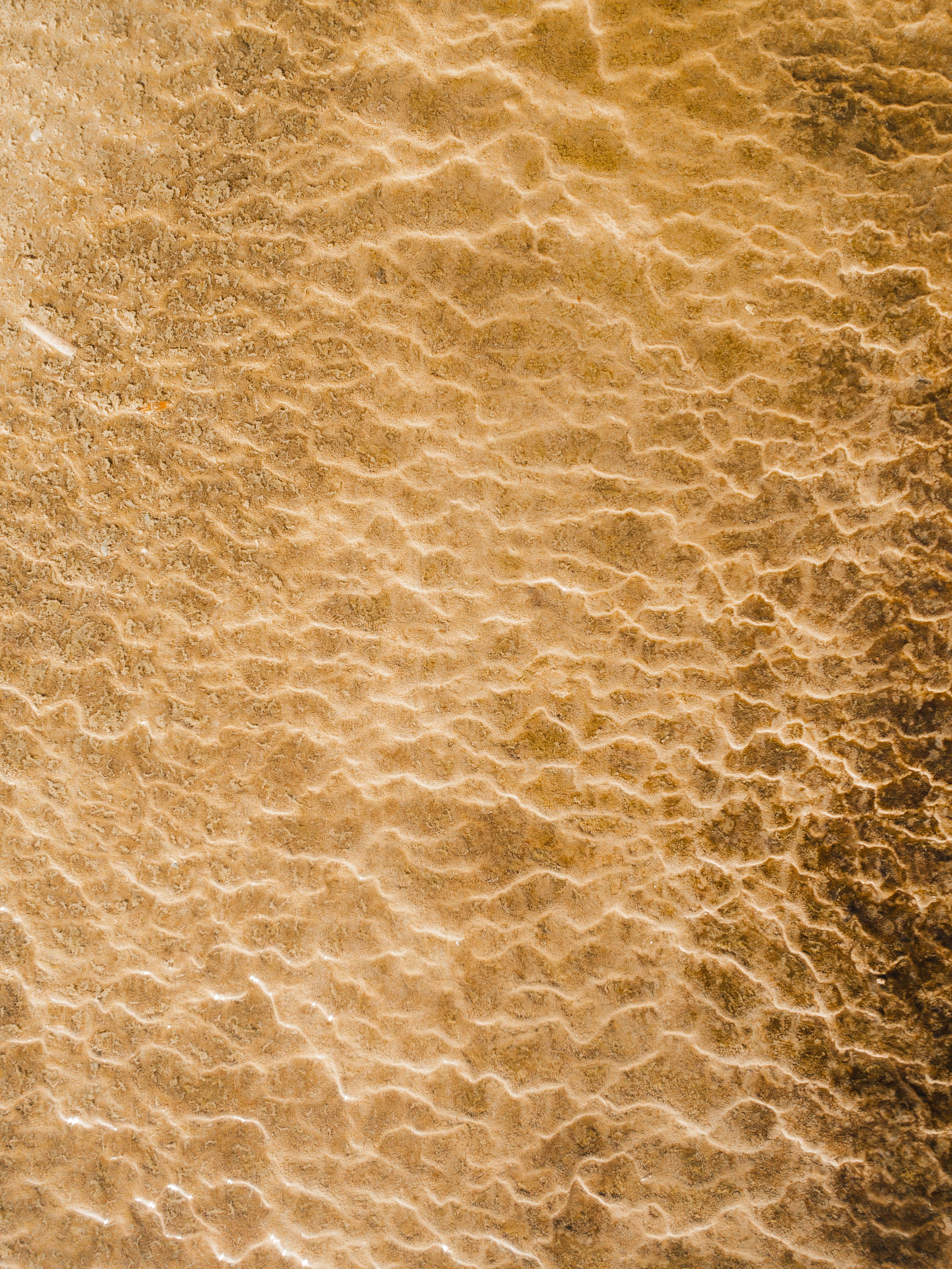 Drone shot of a rippling sand texture on a beach shore with foam patterns.