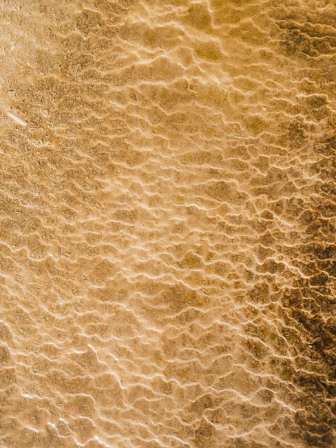 Drone shot of a rippling sand texture on a beach shore with foam patterns.