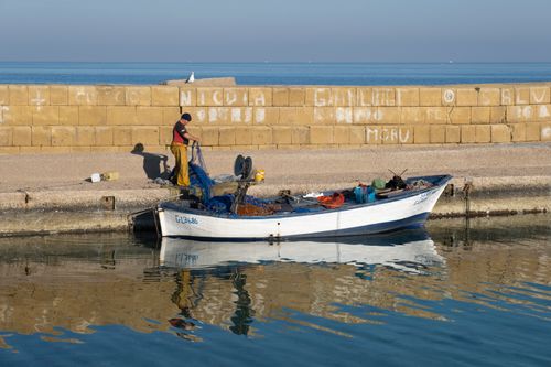Free A fisherman manages nets by a docked boat in Gallipoli, Italy on a bright day. Stock Photo