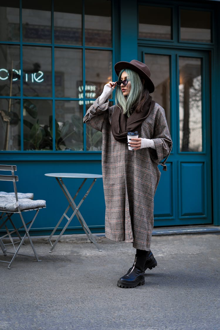 Woman In Brown Coat Wearing Brown Fedora Hat While Walking Outside An Establishment