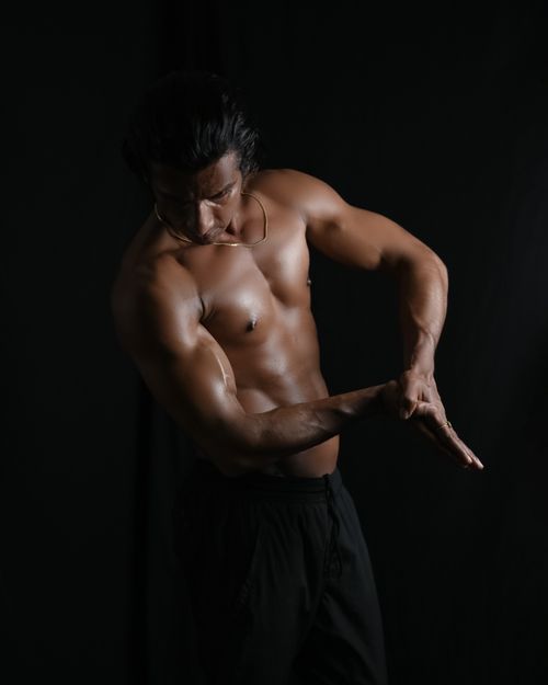 Free Shirtless man in a fitness pose against a dark background, showcasing strength and masculinity. Stock Photo