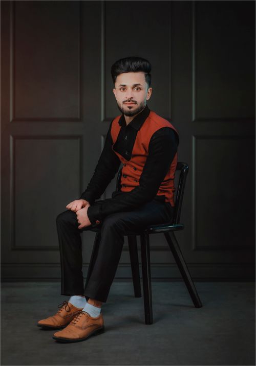 Free Stylish man in formal wear sitting on a chair with a poised expression against a dark background. Stock Photo