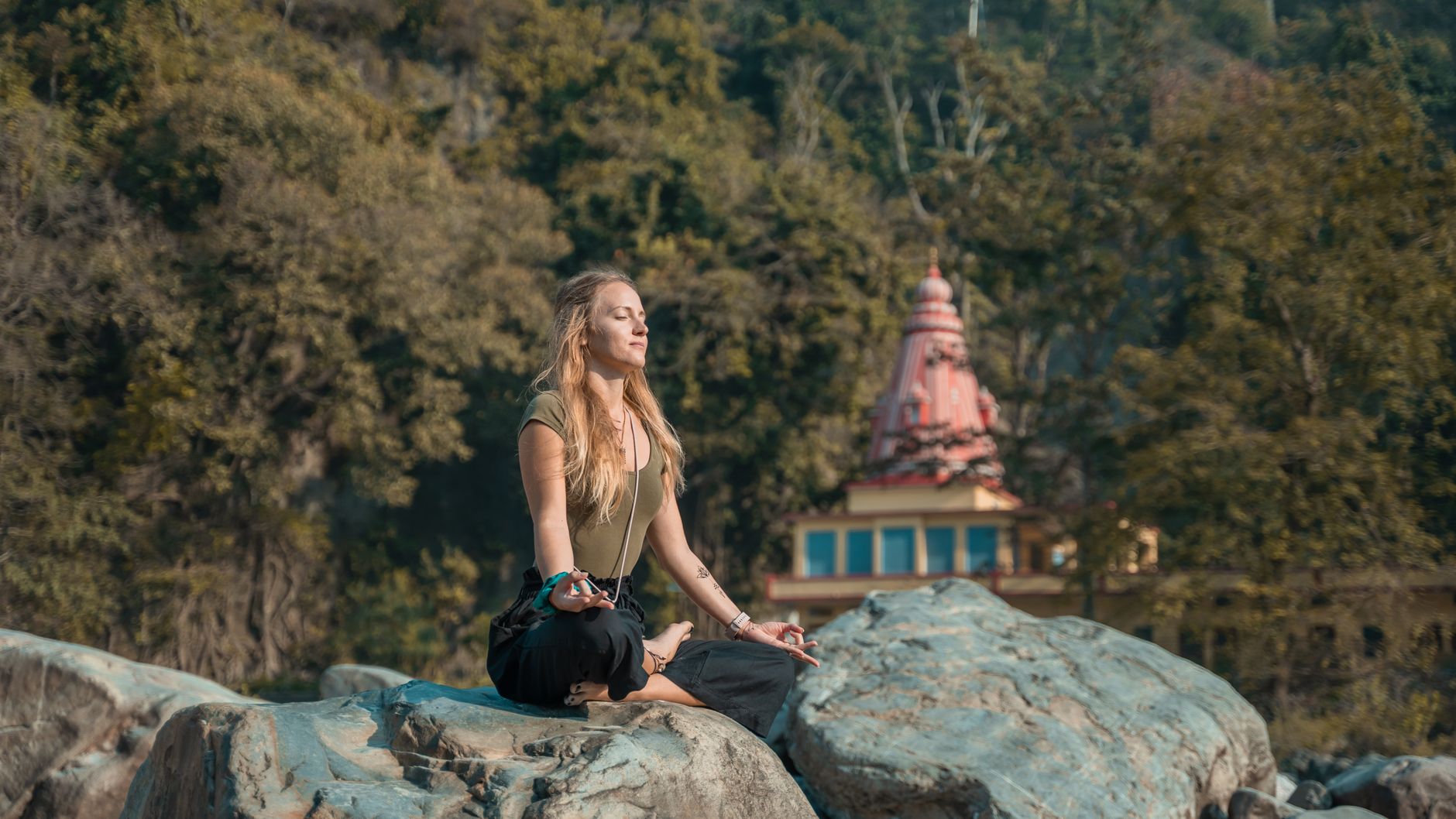 A woman practices yoga on rocky terrain in Rishikesh, India, embracing peace and relaxation.