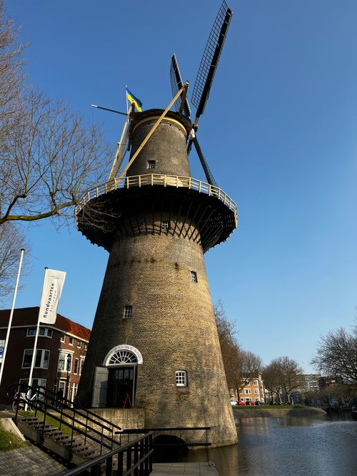 Free Vertical shot of a historic windmill by the riverside on a clear day. Stock Photo
