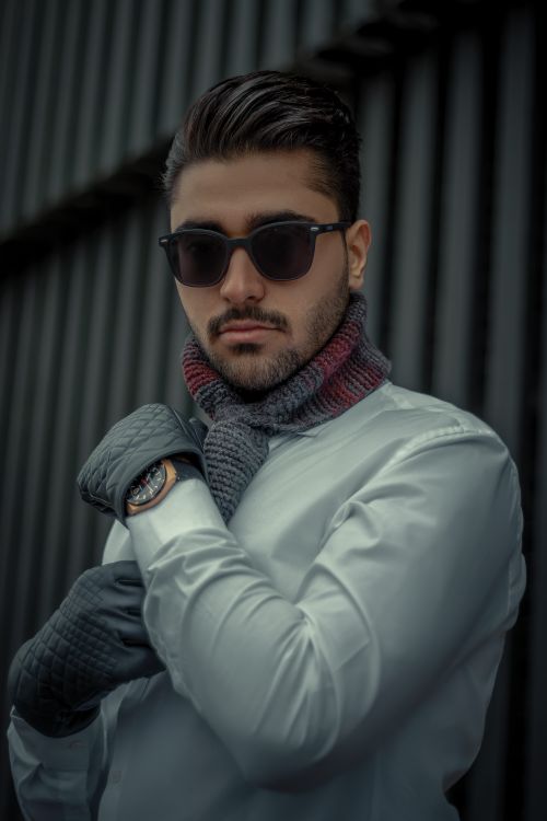 Free Fashionable young man with sunglasses and scarf posing confidently outdoors. Stock Photo