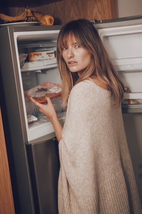 Free A Woman in Sweater Getting Food in the Refrigerator while Looking at the Camera Stock Photo