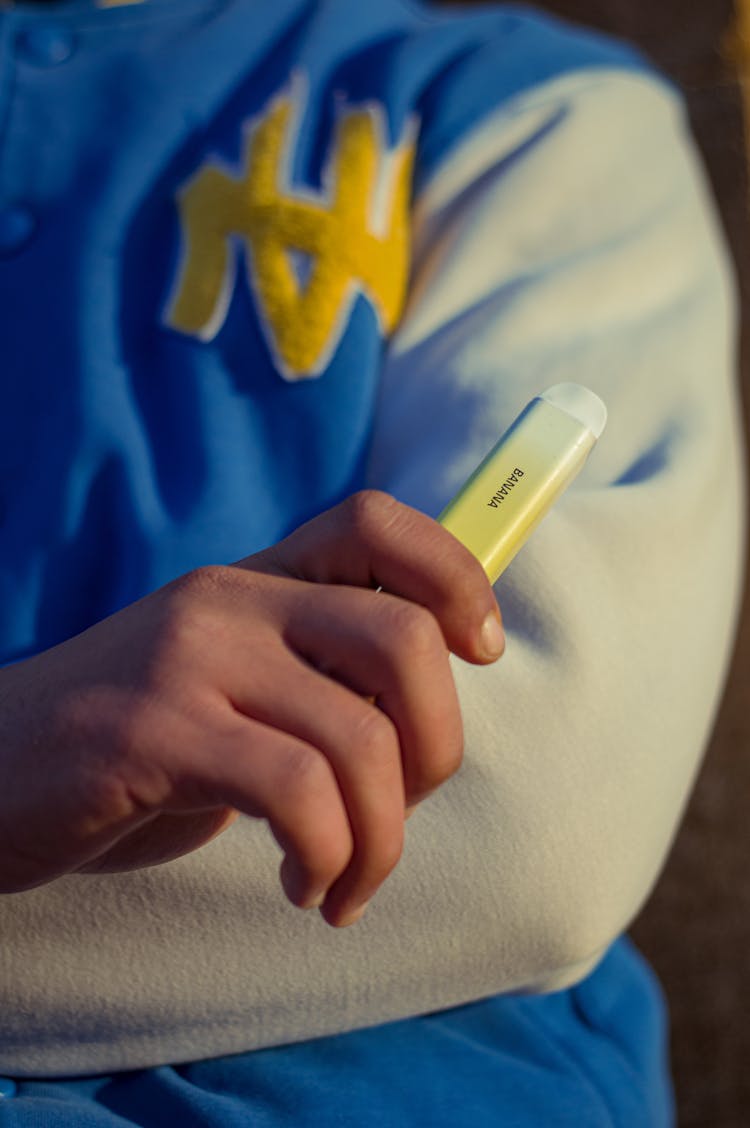 A Person In Blue And White Jacket Holding A Vape