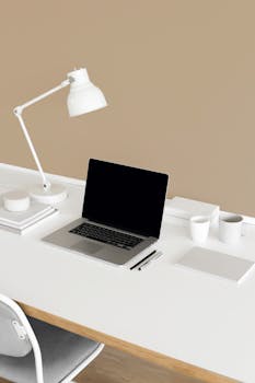 Elegant and clean home office setup featuring a laptop, lamp, and stationery on a modern desk.