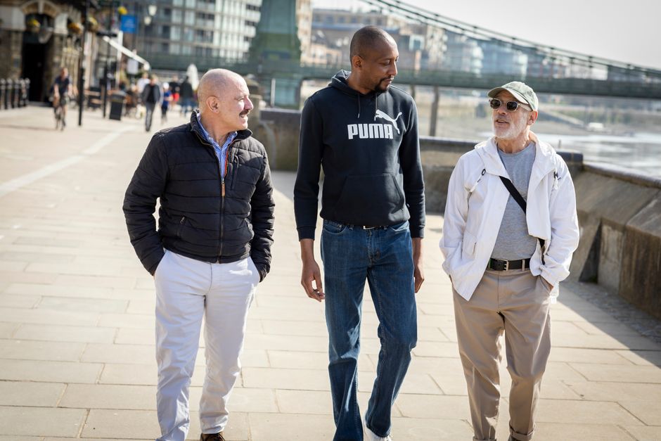 Three men chatting and walking on a riverside promenade in the city.