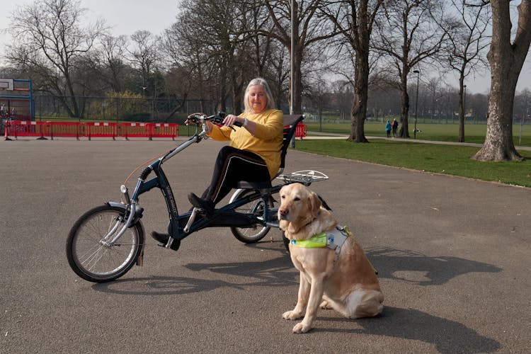 Elderly Woman On A Bike For Disabled People With A Guide Dog