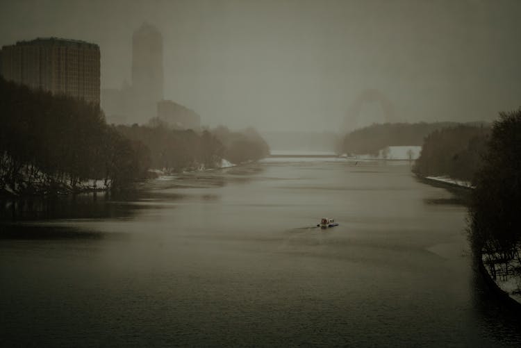 Drone Shot Of A Boat Sailing On The River Surrounded With Green Trees In The City