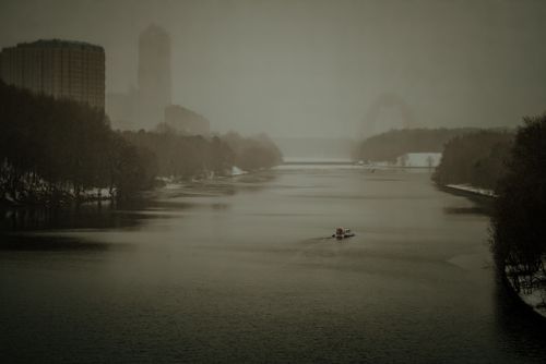 Free A serene view of a misty river in Moscow with a small boat and urban skyline. Stock Photo