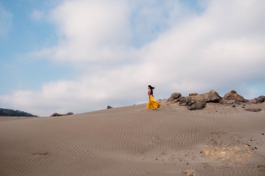 A woman in a yellow dress walking on the sandy dunes under a blue sky in Veracruz.