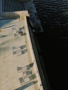Aerial view of empty benches casting long shadows along a waterfront promenade.