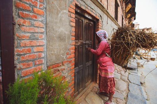 Woman entering in a Wooden Doorway while carrying a Basket full of Twigs 