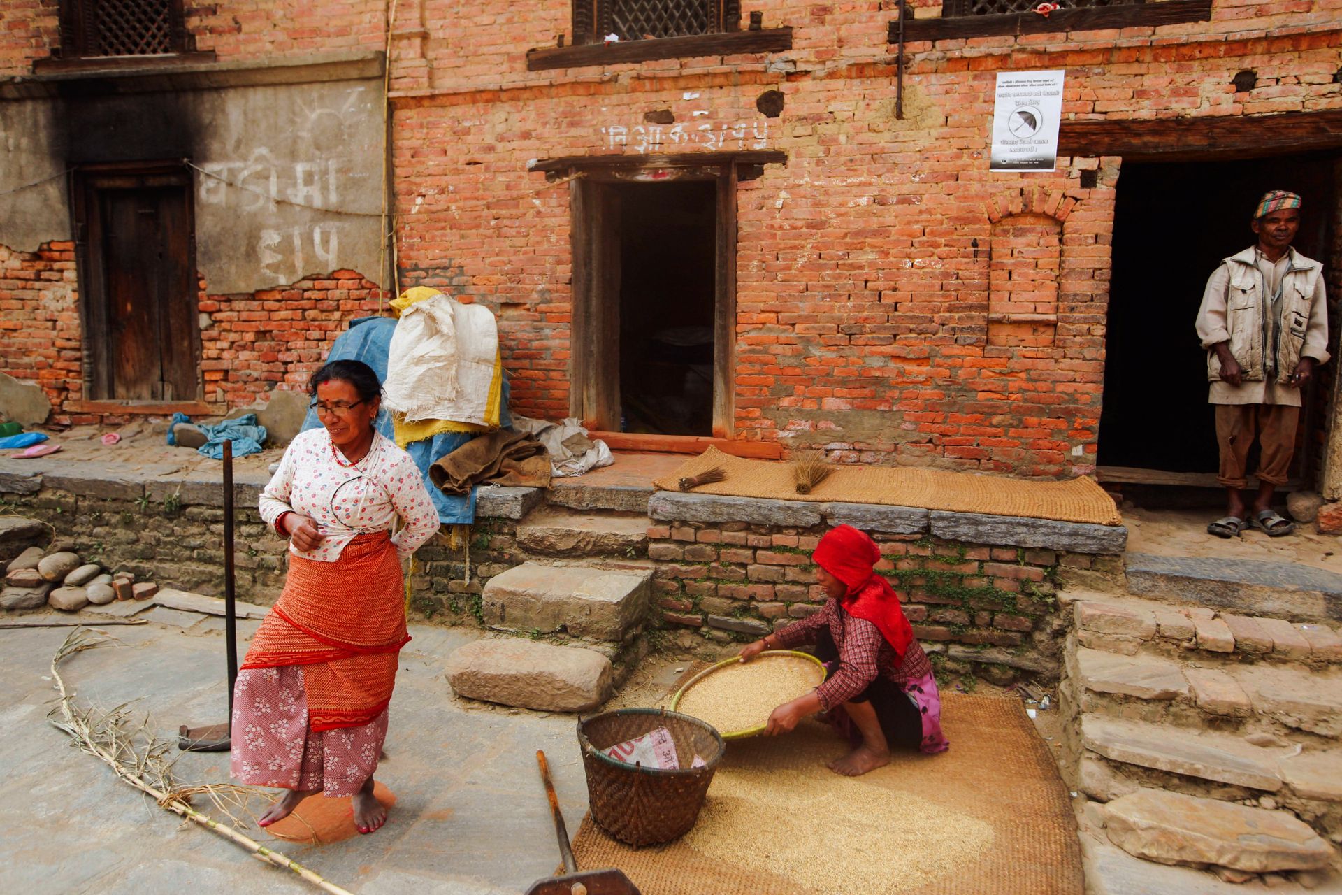People in a rural village sieving grain outdoors, showcasing traditional life and community work.