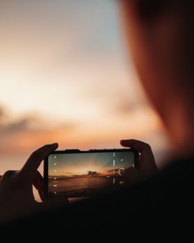 A person photographs a sunset on a smartphone, highlighting a serene outdoor atmosphere.