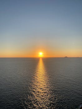 Breathtaking ocean view at sunset with golden sun reflecting on calm sea.
