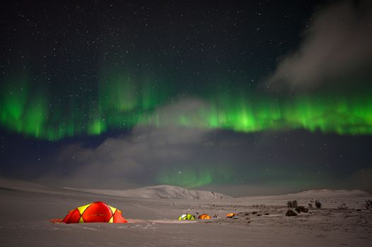 Stunning view of aurora borealis over snow-covered tents in Norway's wilderness at night.