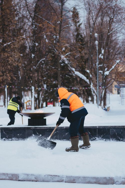 Two workers performing landscaping and snow removal in a park in winter