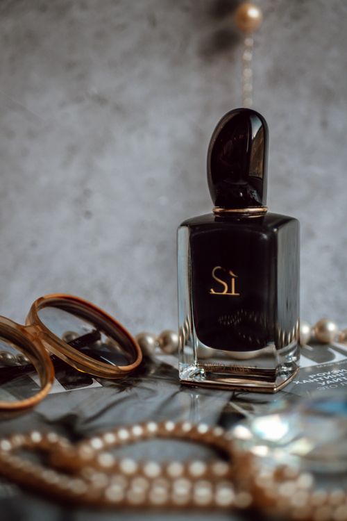 Free Sophisticated setup featuring a black perfume bottle with eyeglasses and pearls on a textured surface. Stock Photo