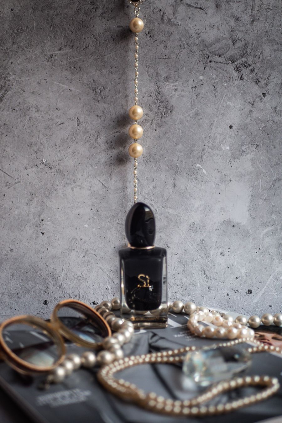 Perfume, pearls, and jewelry arranged on a marble surface