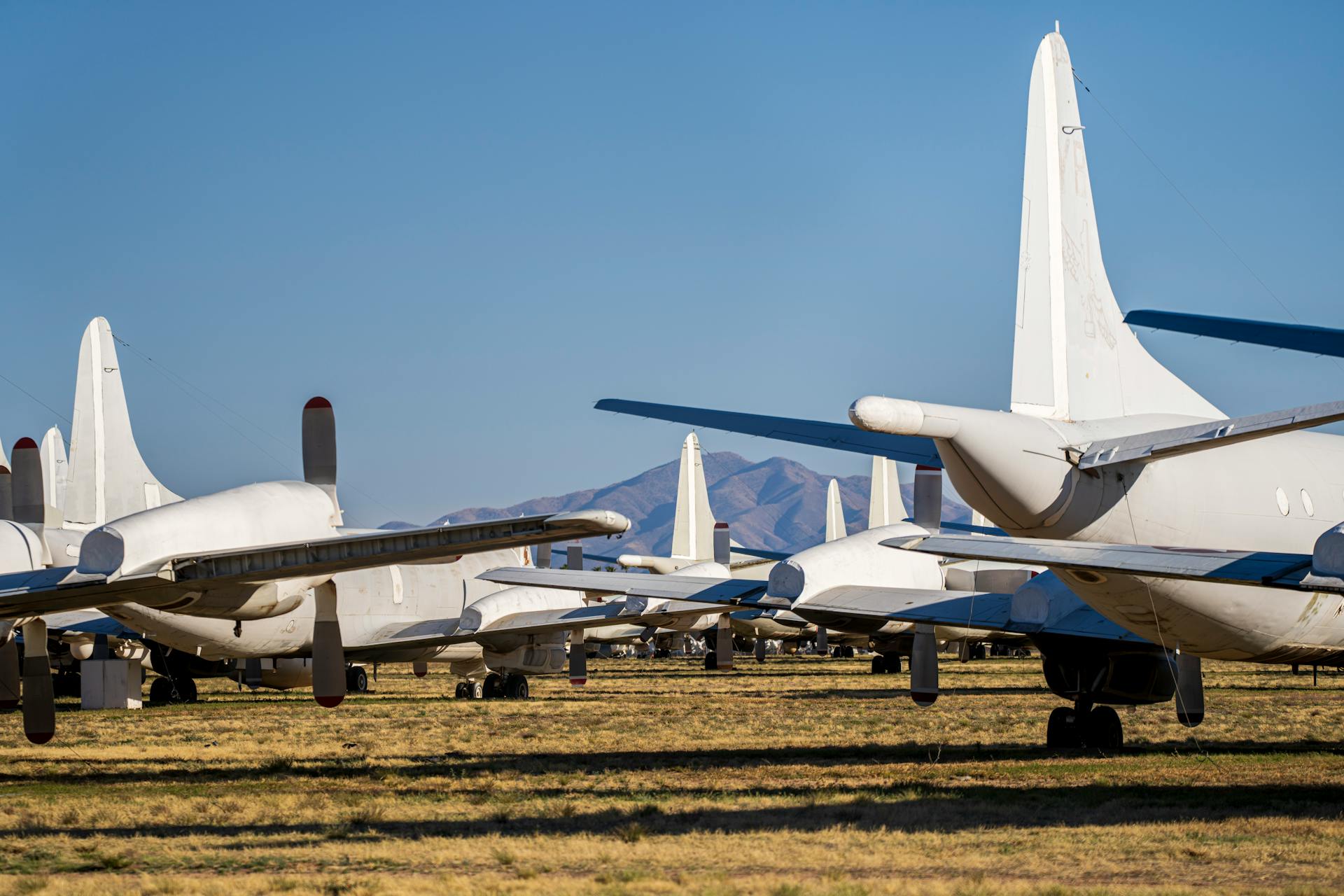 Row of retired aircraft in a desert landscape with mountains and clear sky.