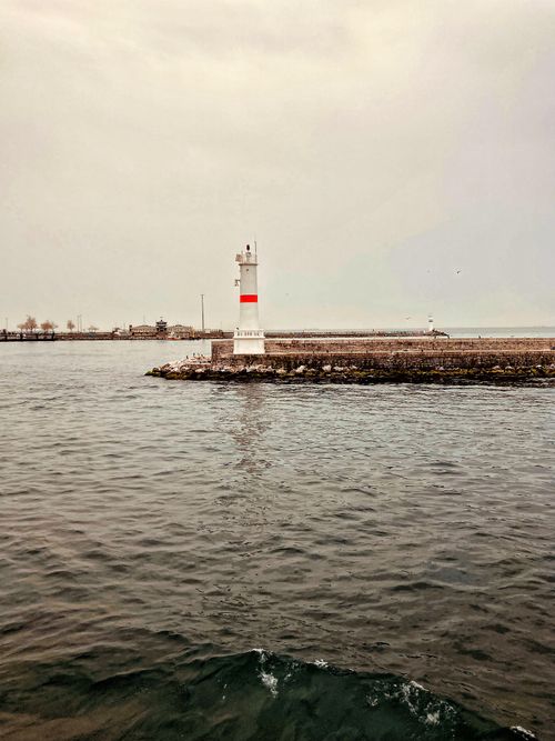 Free A lighthouse stands on a rocky shoreline under an overcast sky, surrounded by calm sea waters. Stock Photo