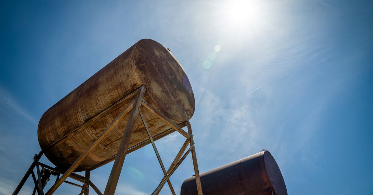 Rusty industrial oil tanks with a clear blue sky and bright sun.