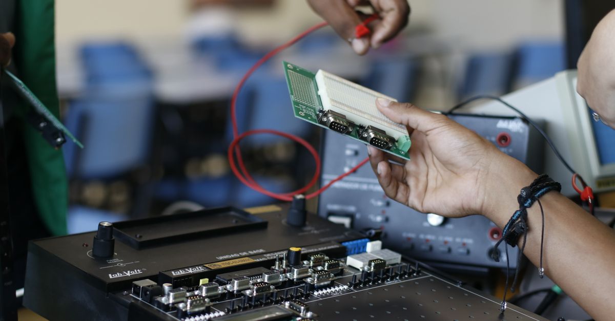 Close-up of hands working with electronics equipment and circuit board in a lab setting.