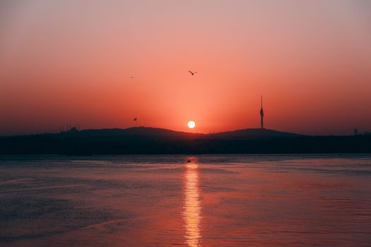 Breathtaking sunset view over İstanbul with silhouettes of hills and water reflection.