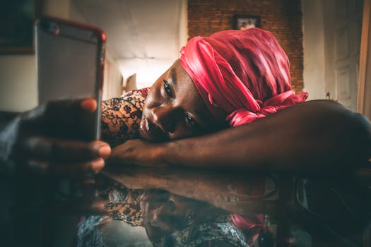 Close-up of a thoughtful African woman lying with a smartphone indoors, wearing a pink headscarf.