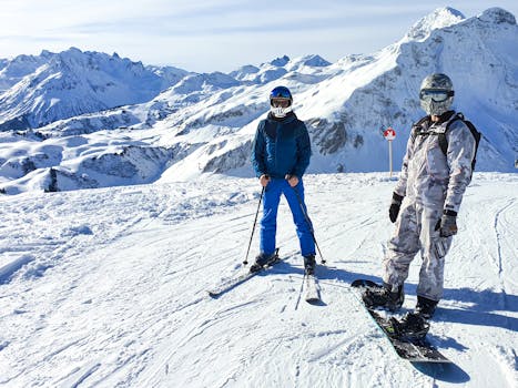 Two adults skiing and snowboarding in the snowy mountains on a sunny winter day.