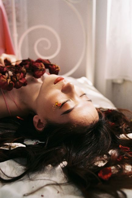 A serene portrait of a woman lying indoors, adorned with dried flowers.