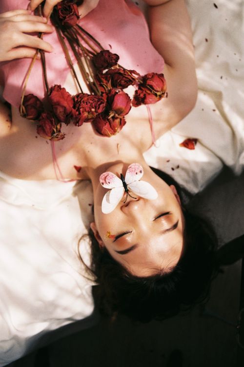 Free Artistic portrait of a woman with a butterfly and withered roses, eyes closed. Stock Photo