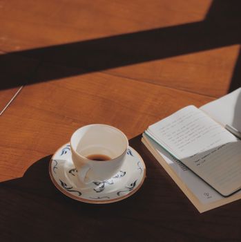 Warm sunlight casts shadows over a coffee cup and open journal.