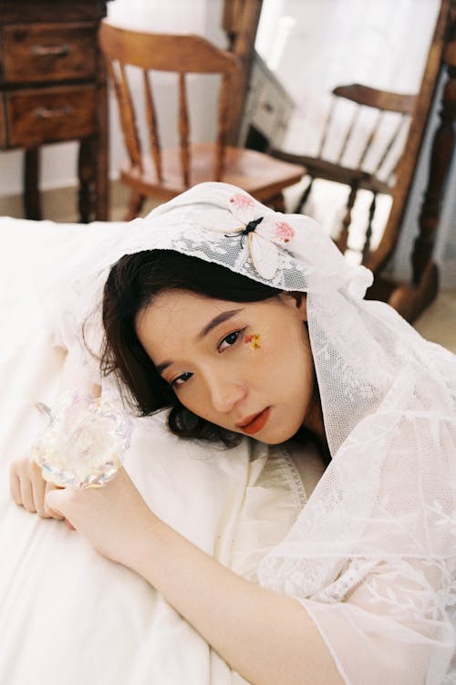 Sad Girl in White Lace Dress Kneeling with Head on Bed