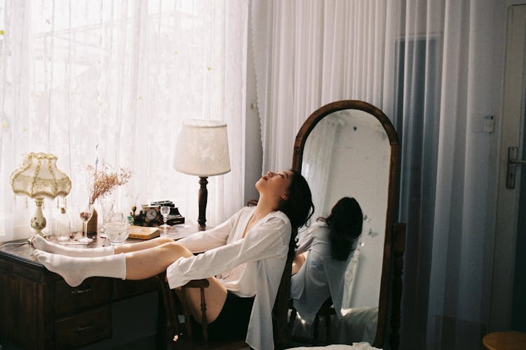 Girl In Bedroom Sitting In Chair with Legs On Backrest