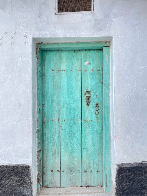 Free A vintage teal wooden door embedded in a rustic, textured concrete wall with a classic knocker. Stock Photo