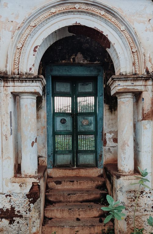 Free Rustic archway entrance with a worn blue door and aged stone columns. Stock Photo