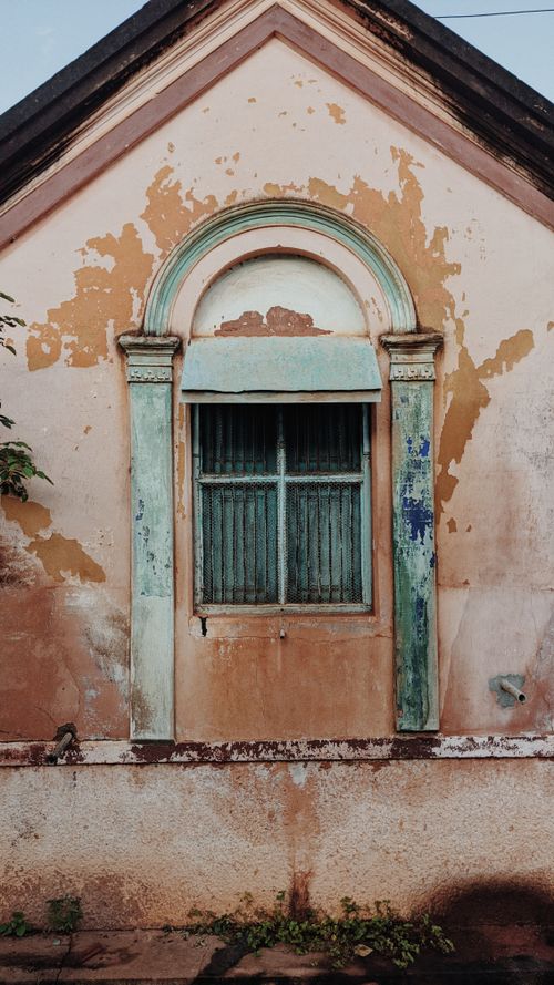 Free A rustic vintage building facade with peeling paint and an arched window, capturing urban decay. Stock Photo