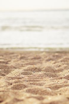 Close-up of textured beach sand with ocean in the blurred background.