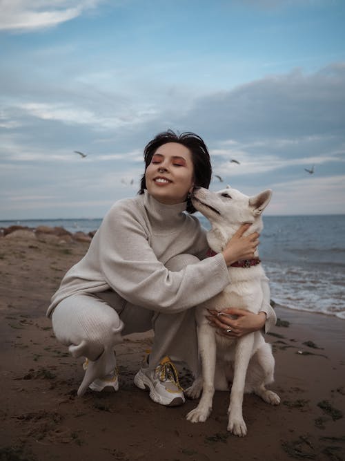 Free Woman in White Robe Sitting on Beach With White Short Coat Dog Stock Photo